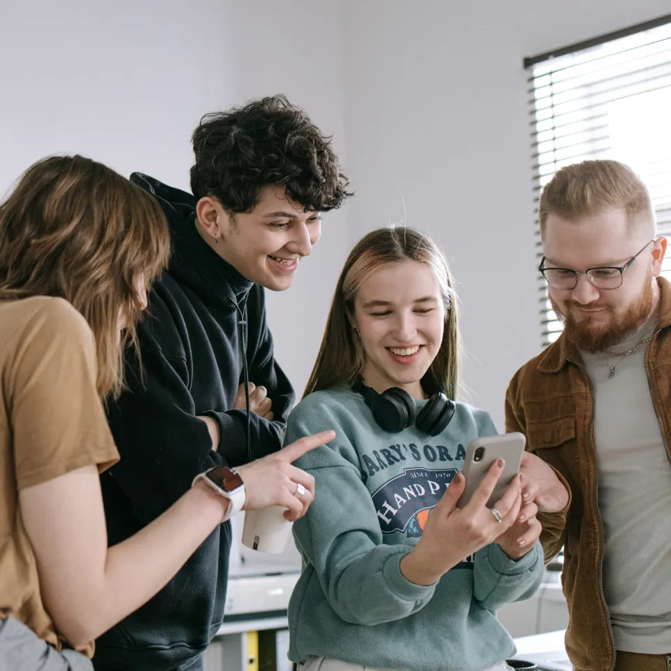 Group of young adults smiling and looking at a smartphone together in a casual indoor setting