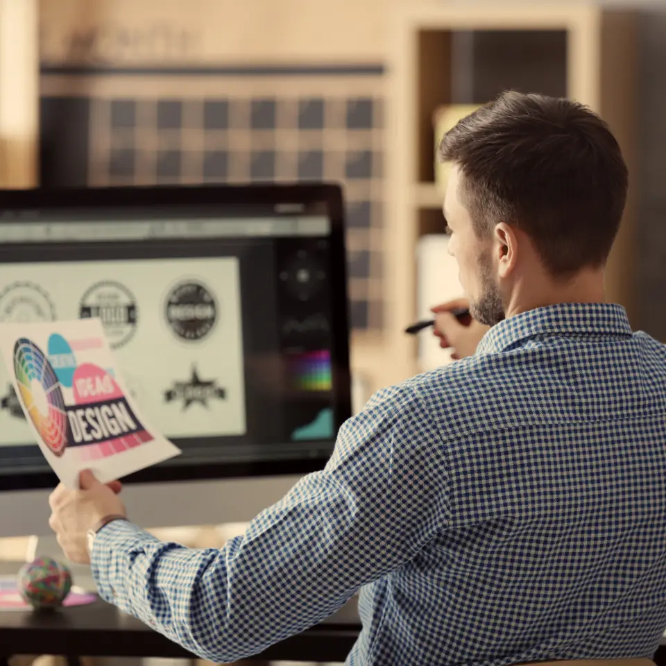 Graphic designer reviewing printed logo concepts while working on logo designs on a desktop computer