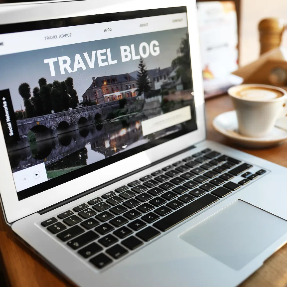 Laptop displaying travel blog website with scenic bridge image and coffee cup on wooden table for blogging concept