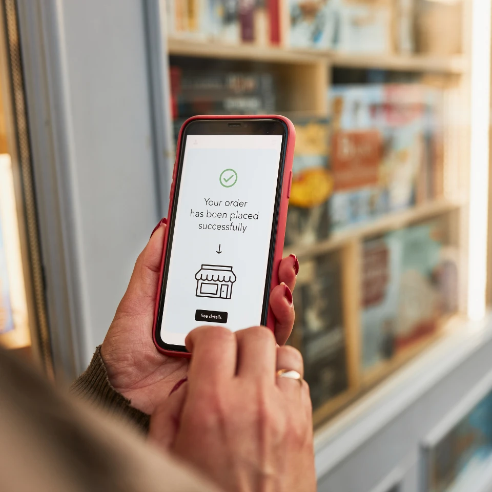 A person holding a smartphone with a confirmation message on the screen that reads Your order has been placed successfully in front of a store bookshelf.
